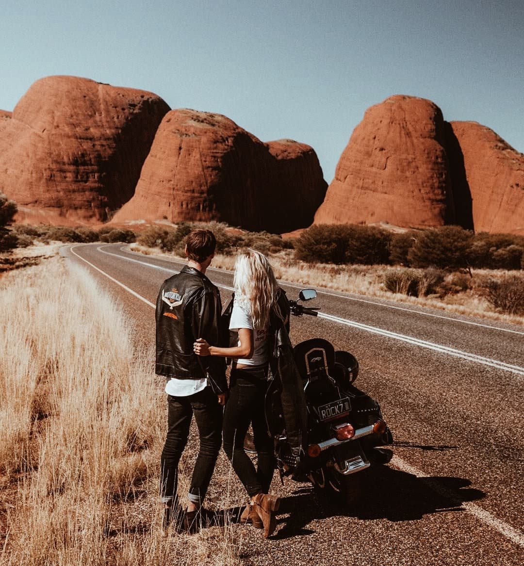 A couple dressed in black leather stands next to a classic Harley looking over North America's richest asset: its western landscapes.