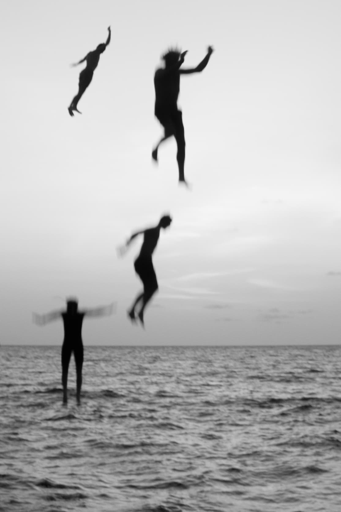 A group of friends jump from the yacht to the ocean.