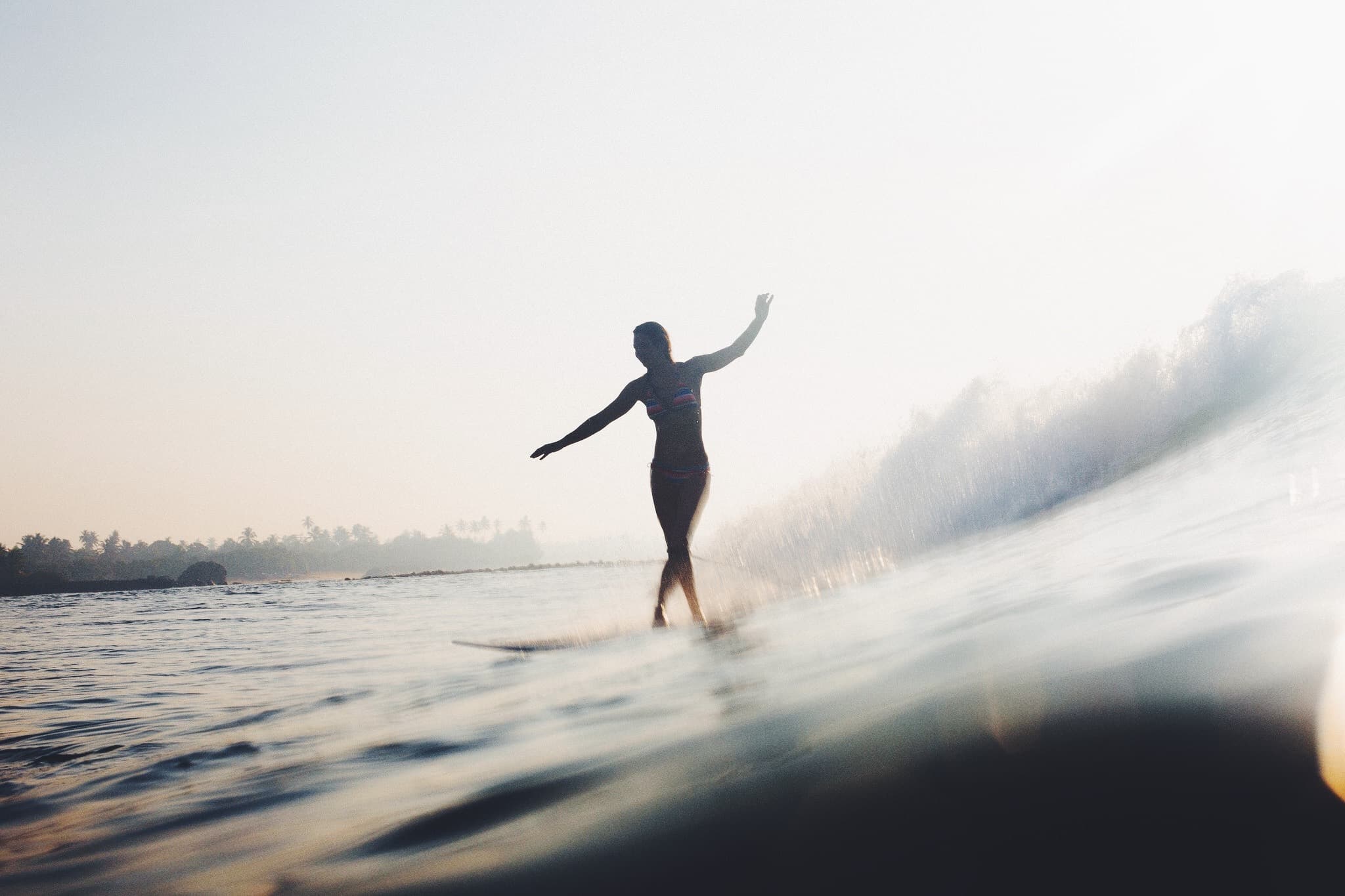 Girl surfing longboard waves in the Maldives during sunset