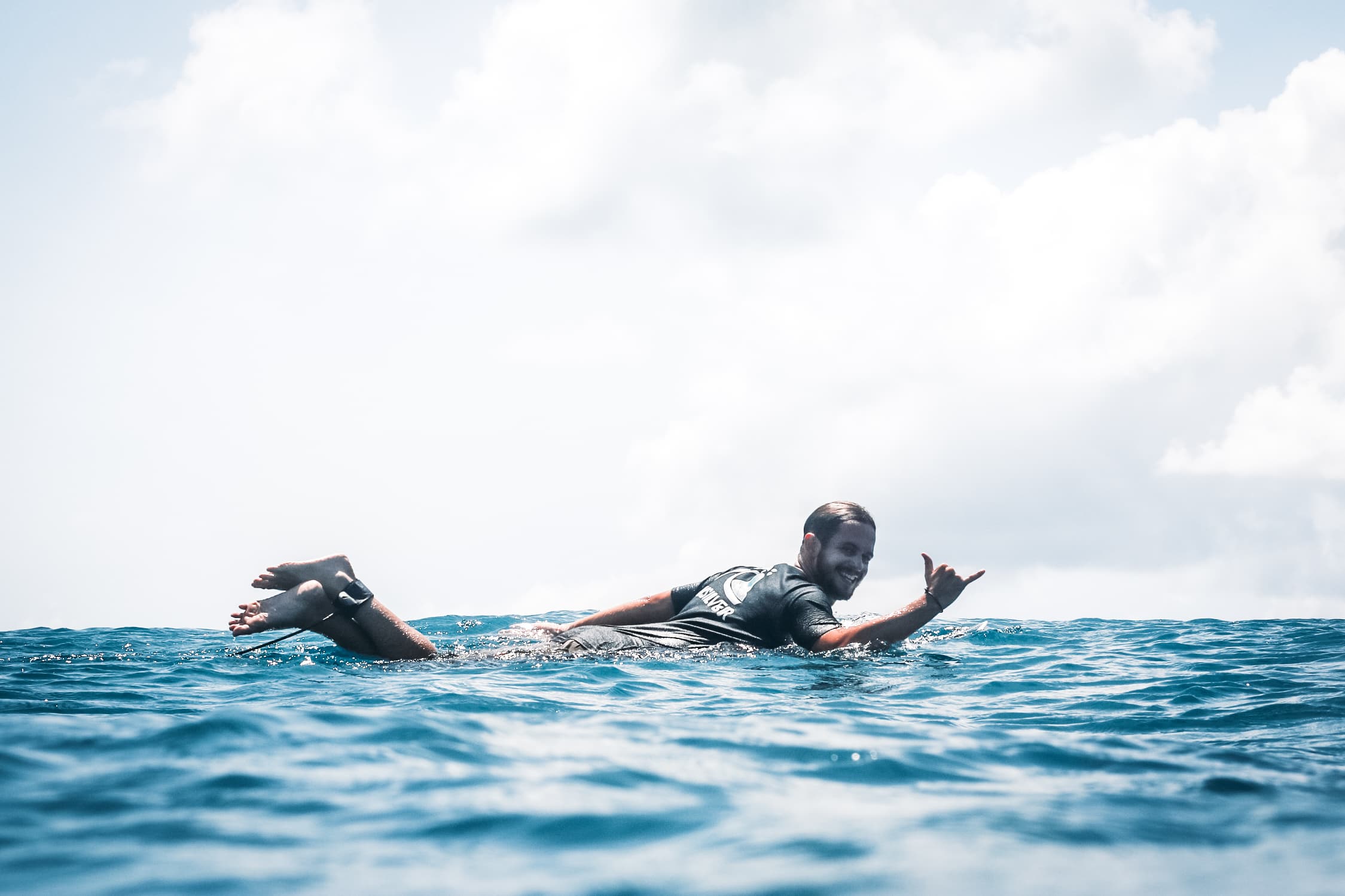 A guy surfing smiles and throws a Shaka to the camera.