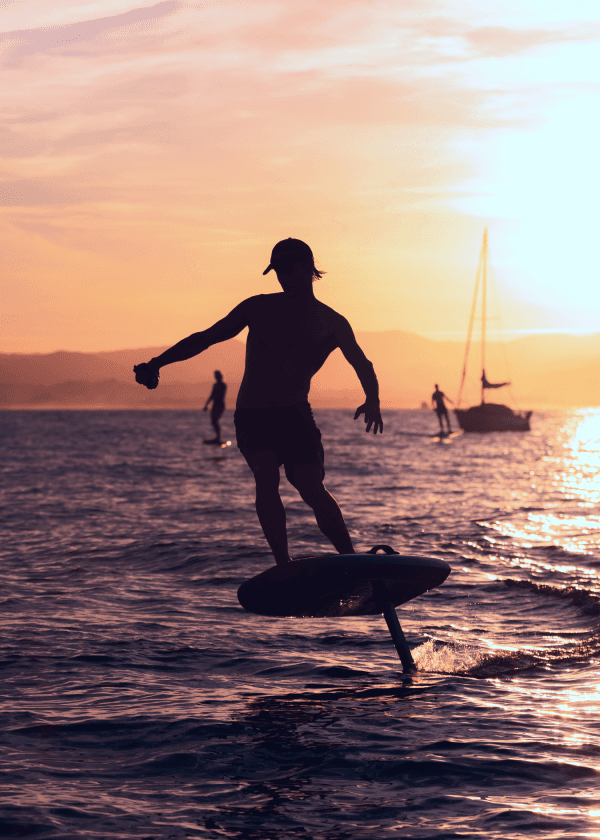Man eFoiling in the ocean next to a sailin yacht at sunset