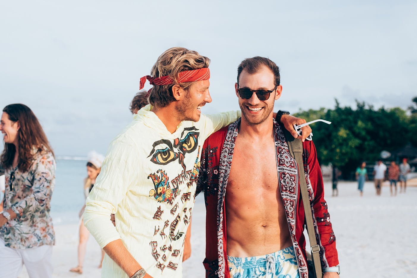 Friends dressed like hippies smile on a private beach in the Maldives. 