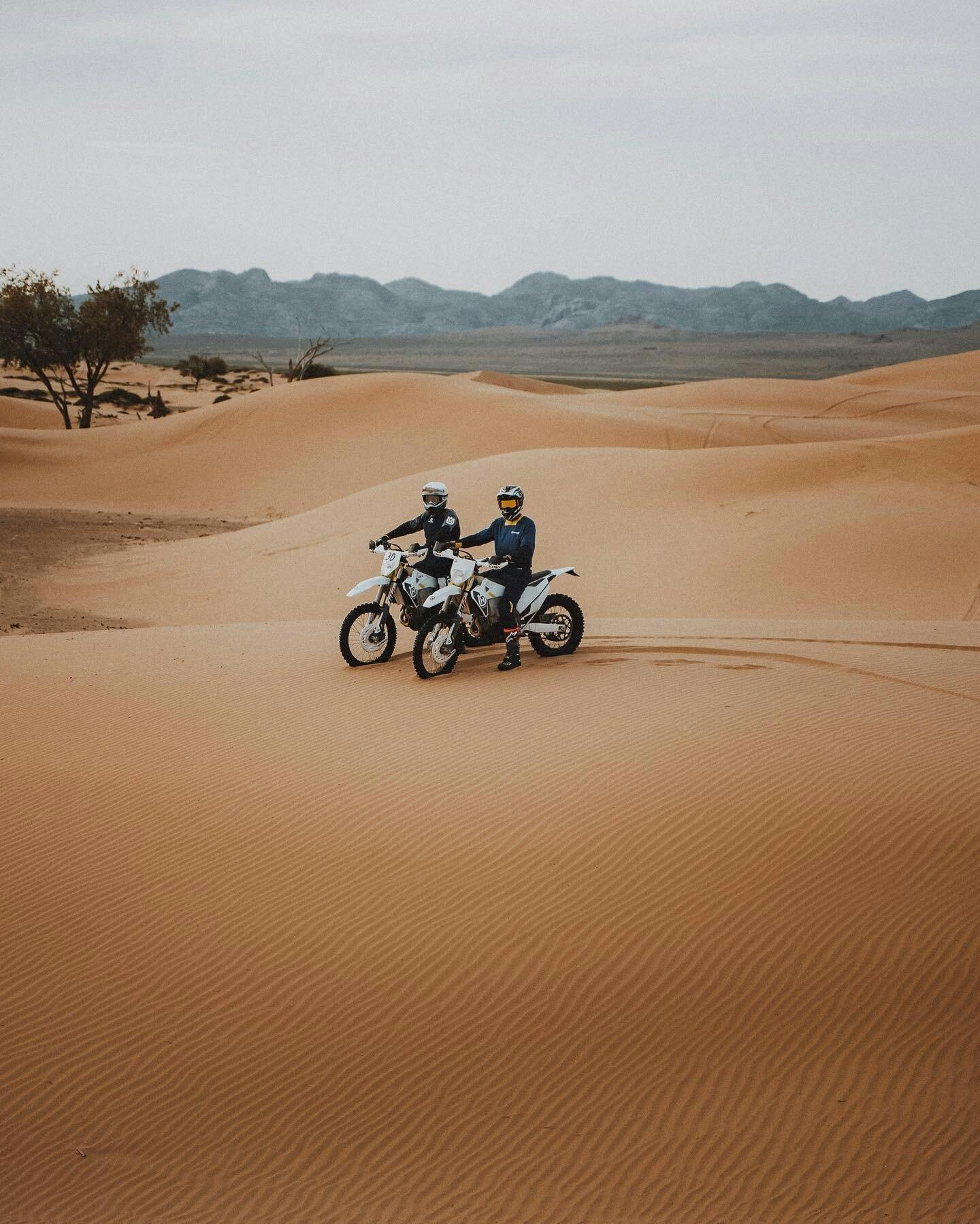 Two friends in the Gobi Desert of Mongolia riding a Husqvarna Enduro motorcycle.