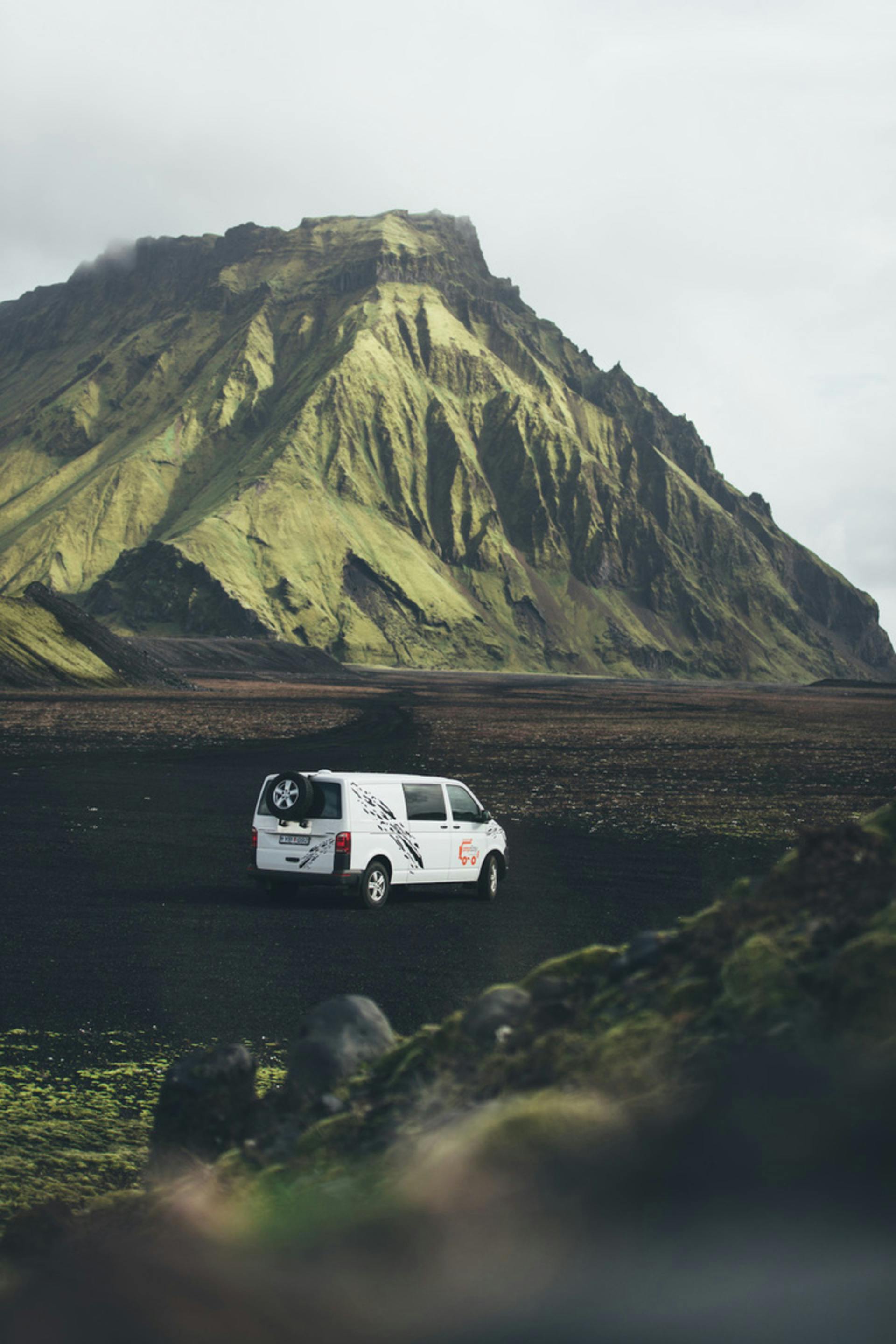 A van sits below a green monumental mountain in Iceland.