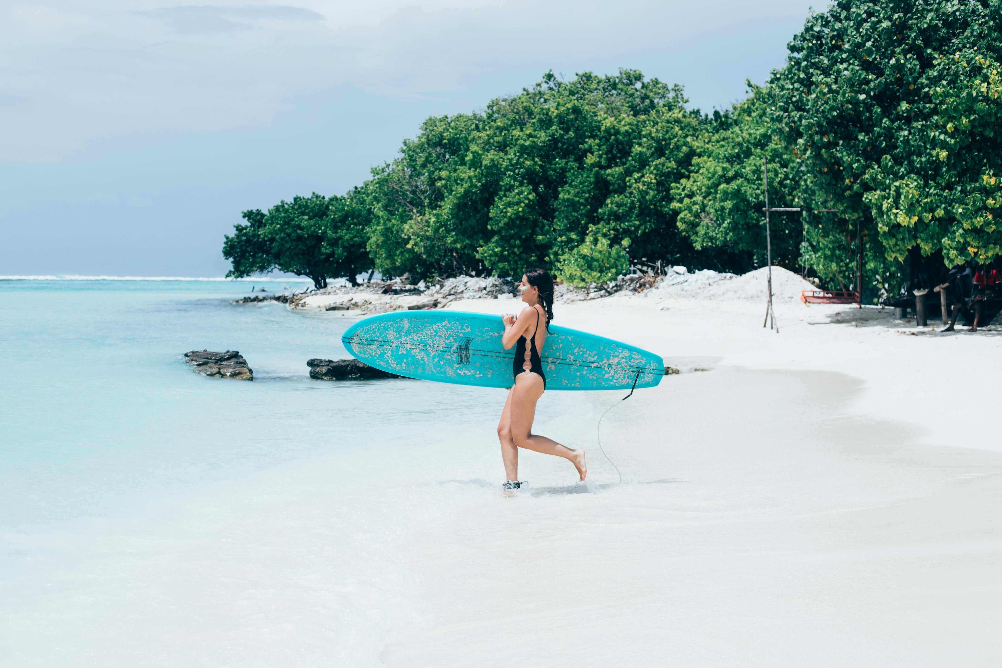 Girl running to the ocean with her surfboard in the Maldives